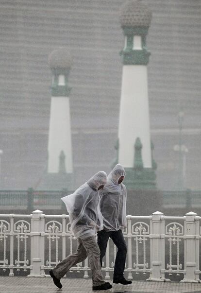 Unos peatones se protegen con chubasqueros de una fuerte tormenta en la capital donostiarra. El temporal de oleaje que azota la costa vasca ha golpeado con fuerza el litoral guipuzcoano, con una altura media de ola de 9,37 metros en San Sebastián, pero, una vez pasada la pleamar de la tarde, no ha dejado daños de gravedad. 