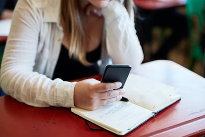 Imagen recortada de una mujer usando un teléfono inteligente en su escritorio en un aula de la universidad.