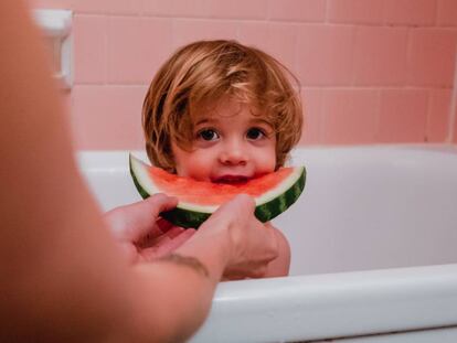 Un niño come un trozo de sandía, mientras se baña.