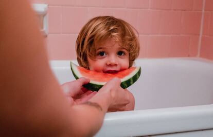 Un niño come un trozo de sandía, mientras se baña.