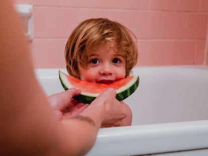 Un niño come un trozo de sandía, mientras se baña.