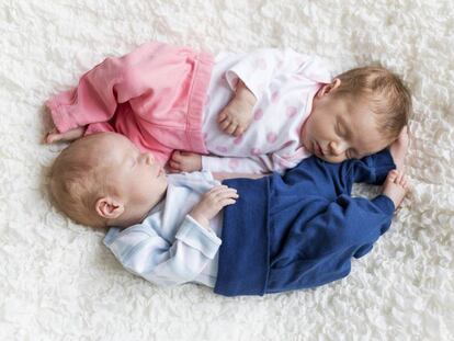 Dos hermanos duermen sobre una manta blanca.