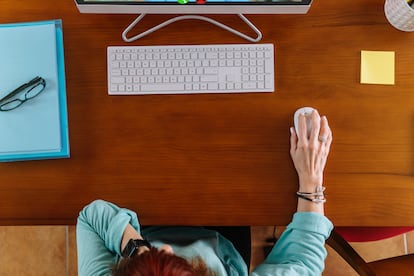 Aerial view of a woman using the mouse of a computer while teleworking in a desk at home