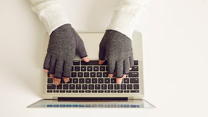 Una persona tecleando un ordenador con los guantes puestos.