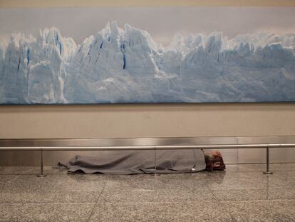 Un hombre duerme debajo de una enorme fotografía de un paisaje muy argentino: un glaciar blanco contrasta con la imagen del hombre sin hogar.