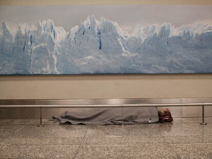 Un hombre duerme debajo de una enorme fotografía de un paisaje muy argentino: un glaciar blanco contrasta con la imagen del hombre sin hogar.