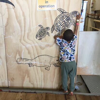 Aisan, de 3 años, pinta con una tiza en un tablerillo decorado con animales en la cubierta de mujeres.