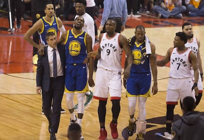 Kevin Durant, es atendido por el jugador de Toronto Raptors Serge Ibaka y su compañero de equipo Andre Iguodala, mientras abandona la pista de juego.