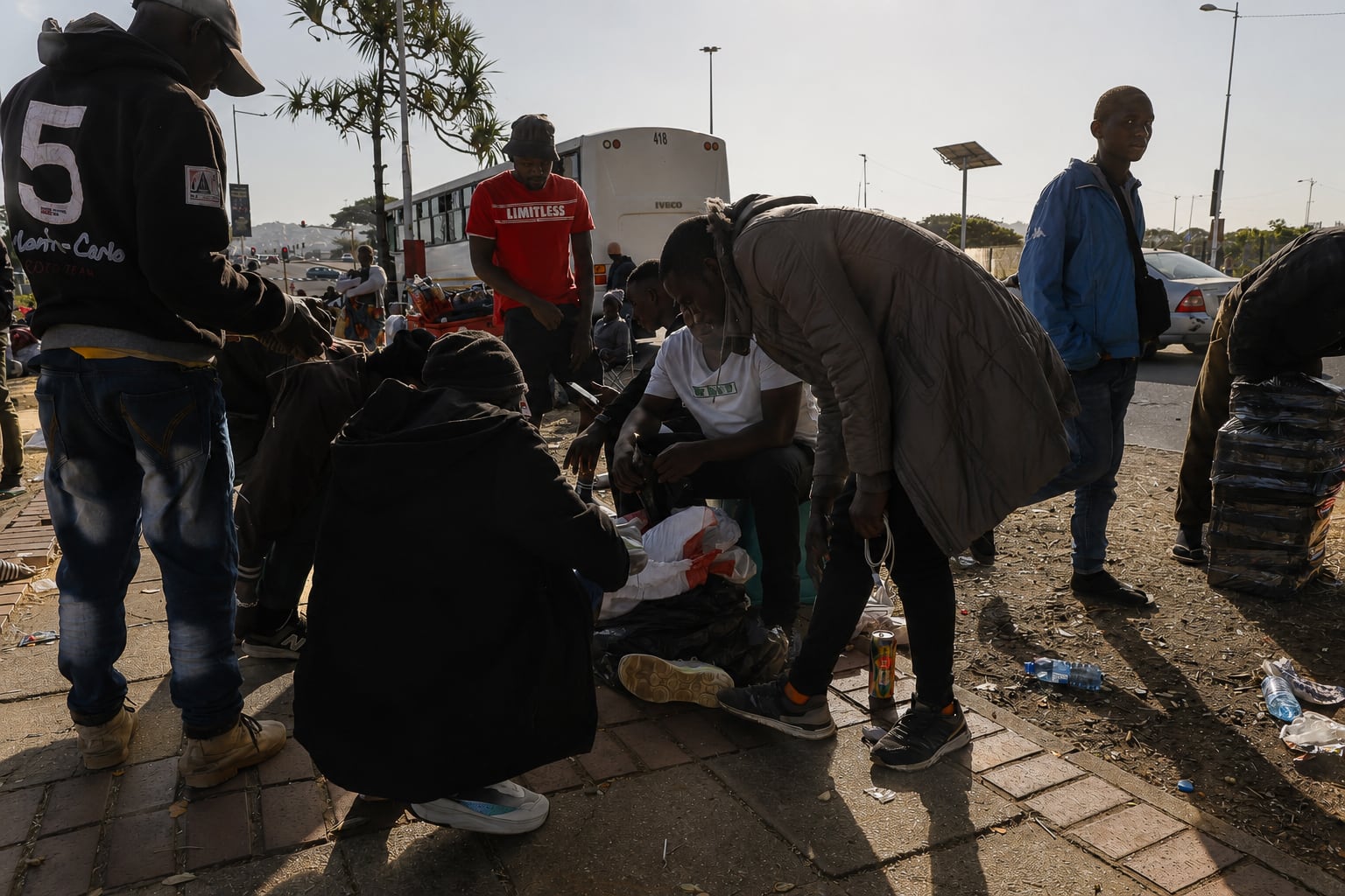
Jackson, inmigrante malauí, vende zapatillas de segunda mano a un grupo de compatriotas que, como él, esperan a ser devueltos a su país en autobús, en un descampado junto a una carretera en Durban (Sudáfrica) el 5 de julio de 2026. 