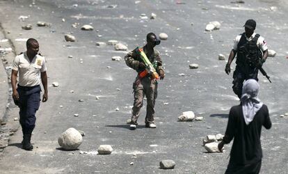 Un manifestante lleva un arma de juguete durante una protesta por la escasez de combustible en Puerto Príncipe (Haití), mientras dos policías pasan junto a él.