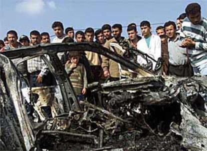 Refugiados de Gaza, junto a los restos del coche en el que  un guardaespaldas de Arafat fue abatido por el Ejército israelí en febrero.