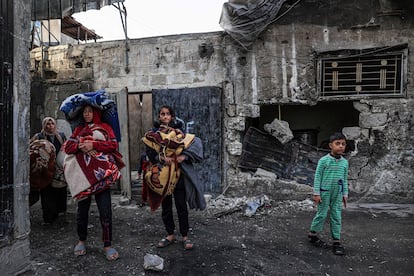 Mujeres y niños palestinos transportan alfombras mientras caminan entre las casas destrozadas a causa de los bombardeos israelíes, este miércoles en Rafah.  