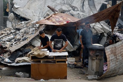 Palestinos preparan comida al lado de un edificio destruido, este lunes en Jan Yunis.  