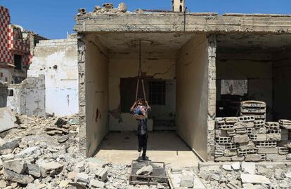 Un niño sirio juega en un columpio instalado en un edificio derruído en Douma, a las afueras de Damasco (Siria).