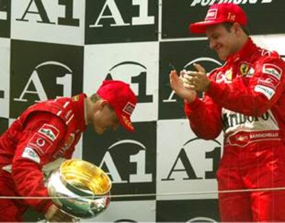 Schumacher se inclina, con el trofeo en la mano, ante Barrichello, que aplaude desde lo alto del podio.