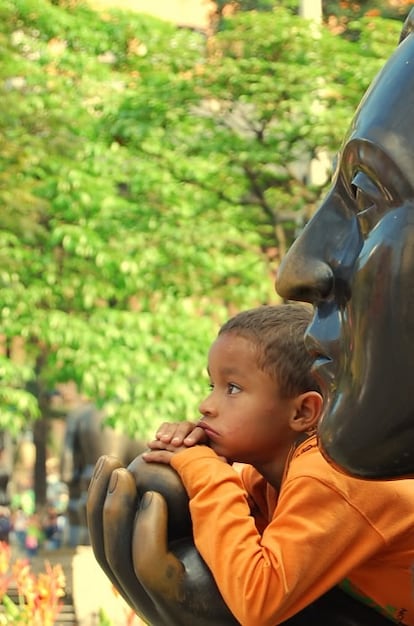 Un niño sueña despierto apoyado en el brazo de una de las esculturas de Botero en la plaza que toma su nombre en el centro de Medellín (Colombia).