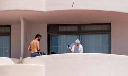 Un joven que permanece en aislamiento en el hotel Palma Bellve, en el balcón mientras personal de limpieza ataviado con un EPI limpia la terraza de la habitación. 