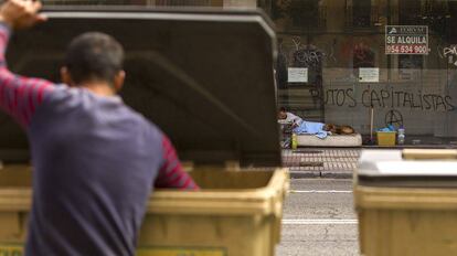 Un hombre busca en la basura delante de un &#039;sin techo&#039; que vive en la calle. 