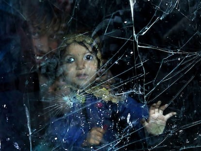 Una niña afgana desplazada mira a través de la ventana de su casa hecha de la luna rota de un automóvil en un barrio de Kabul, Afganistán.