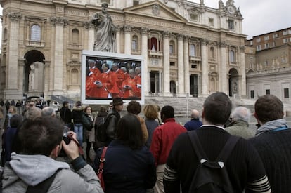 Varios turistas observan la misa desde una pantalla.