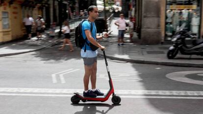 Un usuario conduce un patinete eléctrico por Madrid con el móvil en la mano.