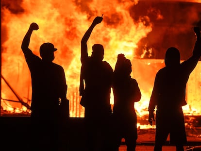 Varios manifestantes alzan el puño junto a una tienda en llamas, durante unos disturbios en Minneapolis, este sábado
