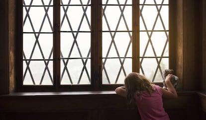 Uma menina espera junto a uma janela.