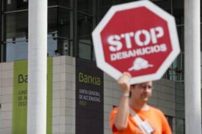 Un hombre sujeta un cartel en protesta por los deshaucios a las afueras del Palacio de Congresos de Valencia donde ayer fue la primera junta de accionistas de Bankia a menos de un mes del primer aniversario de su debut en Bolsa.