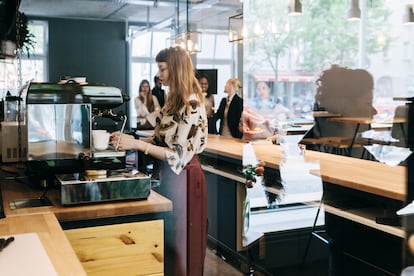 Stylish young waitress preparing coffee for customers in a busy business cafe