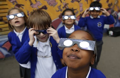 En Londres, varios niños miran el eclipse con gafas.