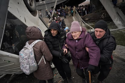 Una anciana es ayudada a cruzar un puente destruido en Irpin, cerca de Kiev, este sábado.
