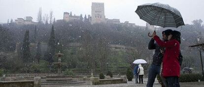 Una pareja se protege de las precipitaciones en Granada con la Alhambra al fondo.