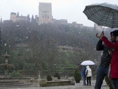 Una pareja se protege de las precipitaciones en Granada con la Alhambra al fondo.