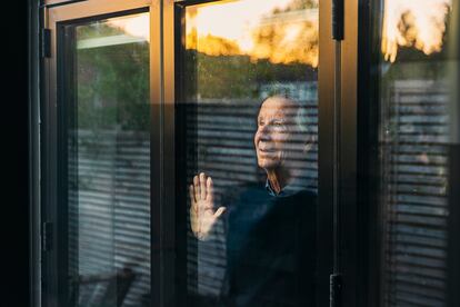 Un hombre mayor mira el atardecer por su ventana.