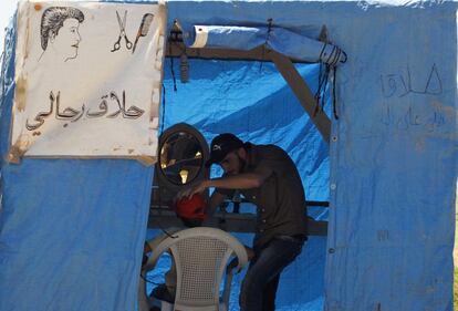 Un barbero sirio atiende a un cliente en la tienda-peluquería de un campo de refugiados de Aleppo junto a la frontera con Turquía. 17 de mayo 2014.