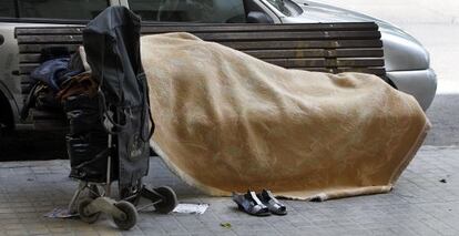 Un indigente duerme sobre un banco p&uacute;blico en Valencia.