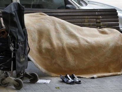 Un indigente duerme sobre un banco p&uacute;blico en Valencia.