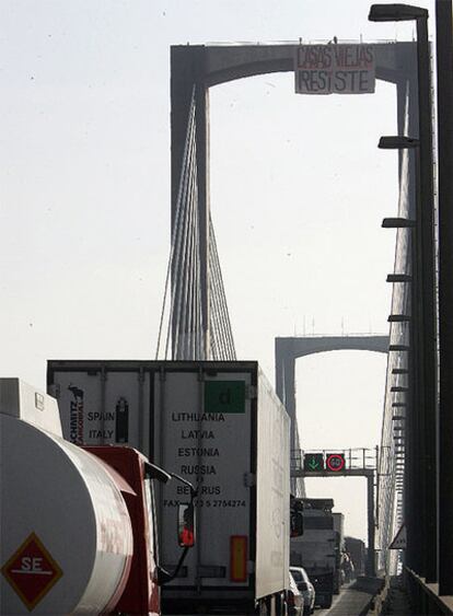 Los dos <i>okupas</i> que se han colgado de una hamaca en el Puente V Centenario de Sevilla despliegan una pancarta.