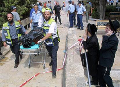 Dos judíos ultraortodoxos miran cómo se llevan en una camilla el cadáver de una de las víctimas del atentado de ayer en Jerusalén.