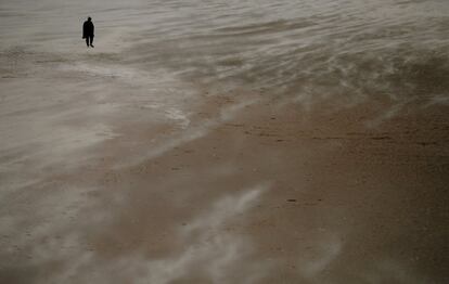 Una mujer camina por la playa a través de la arena que sopla en New Brighton, Gran Bretaña.