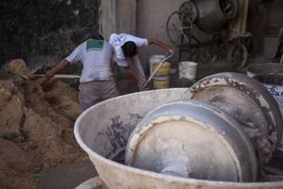 Operários da construção civil preparam mistura de areia e cimento.