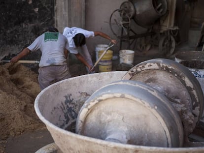 Operários da construção civil preparam mistura de areia e cimento.