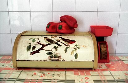 Una panera antigua junto a una báscula y unos pimientos, sobre la mesa de la cocina.