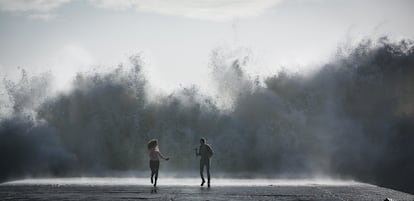 Una pareja corre tras hacerse un selfie mientras pican las olas en el espigón del Bogatell en Barcelona, este jueves.