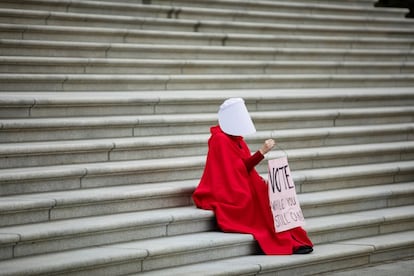 La activista Kelli Midgley, ataviada como las mujeres de El cuento de la criada, sostiene una pancarta en la que se lee "Vota mientras puedas" en protesta contra el presidente Donald Trump.