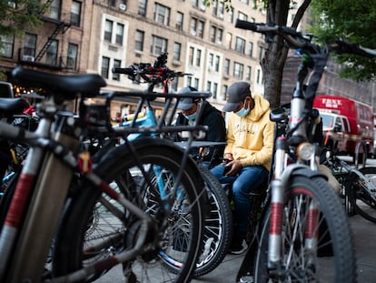 Repartidores de comida a domicilio consultan sus móviles a la espera de un nuevo encargo, en Nueva York.