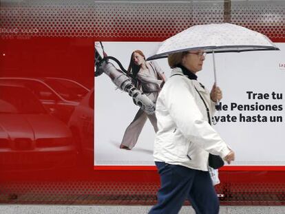 Una mujer camina delante de un cartel que promociona planes de pensiones.