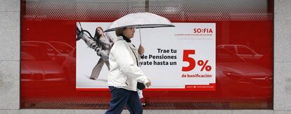 Una mujer camina delante de un cartel que promociona planes de pensiones.