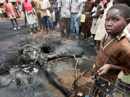 Un niño sujeta su juguete de alambre junto a un cadáver quemado por una turba violenta ayer en Kisumu.