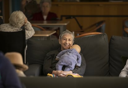 Uno de los muñecos reposa sobre Esther Alonso, que está sentada en uno de los sillones del salón de la residencia. El personal del centro cuenta que la ven nerviosa, yendo de un lado para otro, como buscando algo, y cuando le dan un muñeco se calma. Los reciben por periodos cortos de tiempo.